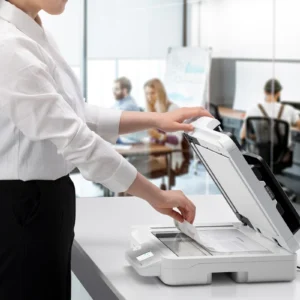 Office worker scans a document on a white desktop scanner in a bright open plan office